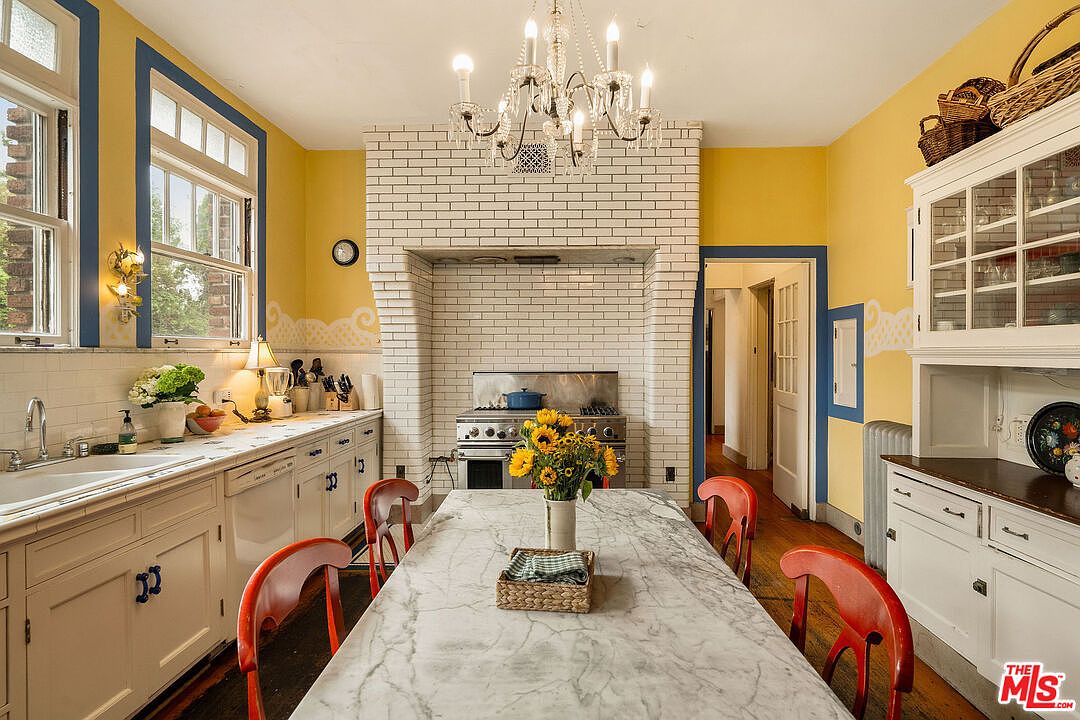 Kitchen with yellow walls, blue window trim, and a marble island with red chairs.